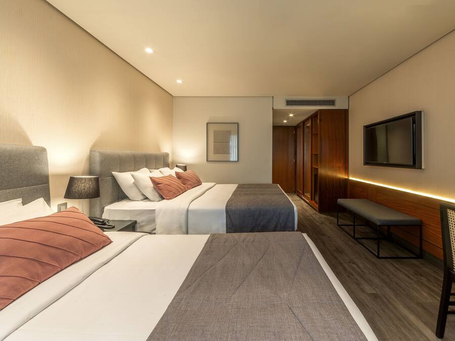 Une chambre d’hôtel avec deux lits, un banc, une télévision et une table de chevet avec une lampe.