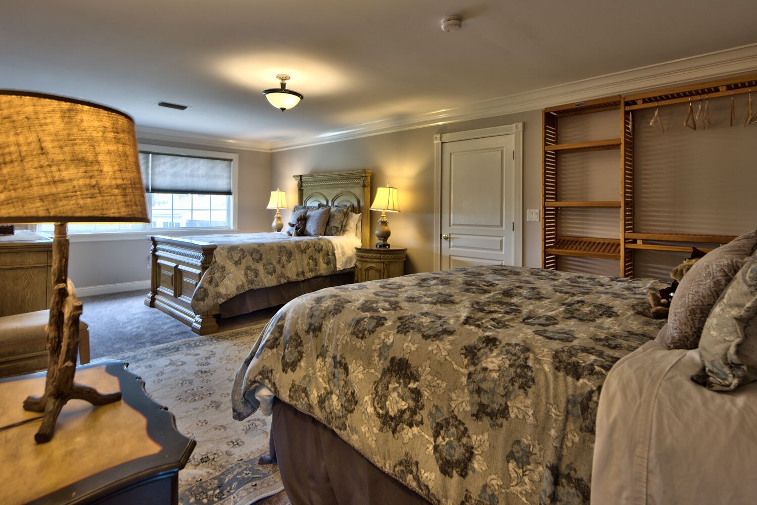 A bedroom with two beds, a wooden wardrobe, a lamp, and a window.
