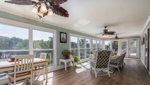 A spacious room with large windows, a dining area with a table and chairs, and ceiling fans.