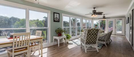 A spacious room with large windows, a dining area with a table and chairs, and ceiling fans.