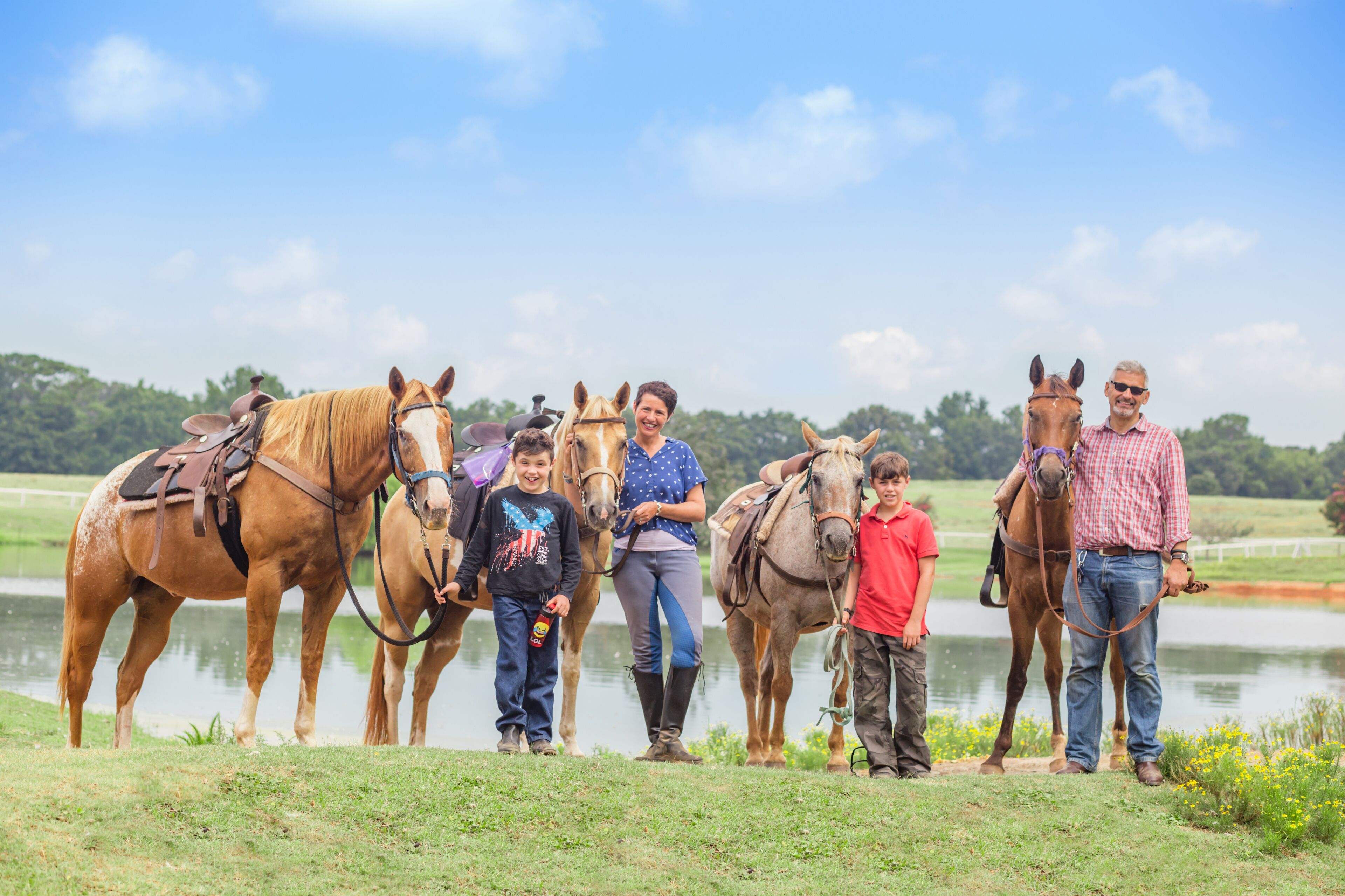 Un groupe de personnes se tient debout, près d’un plan d’eau, avec des chevaux.