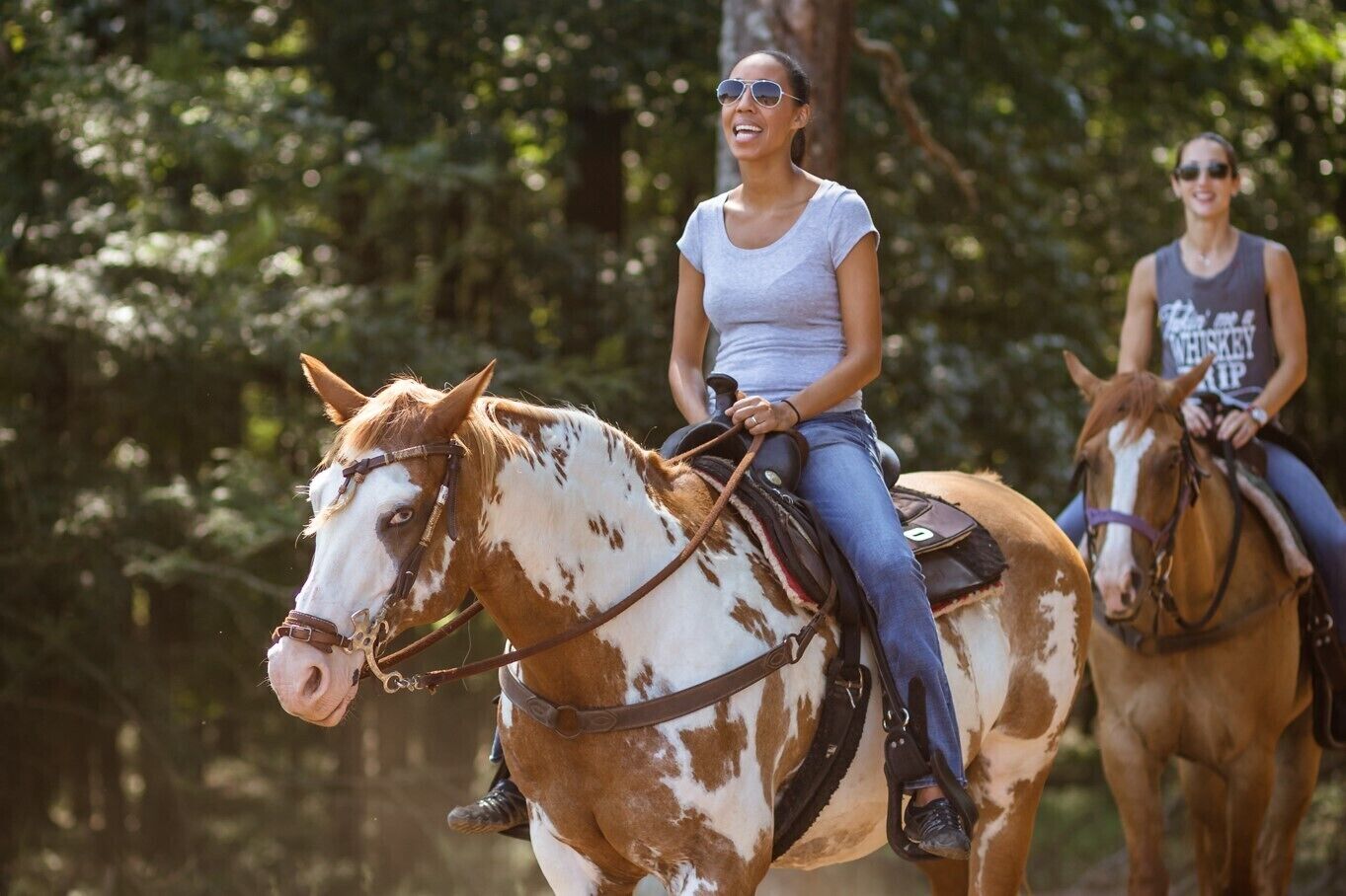 Dos personas montando a caballo en un área boscosa.