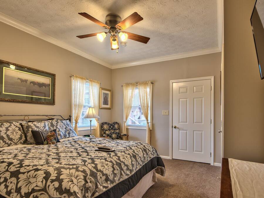 A bedroom with a bed, a ceiling fan, a door, and a window with curtains.