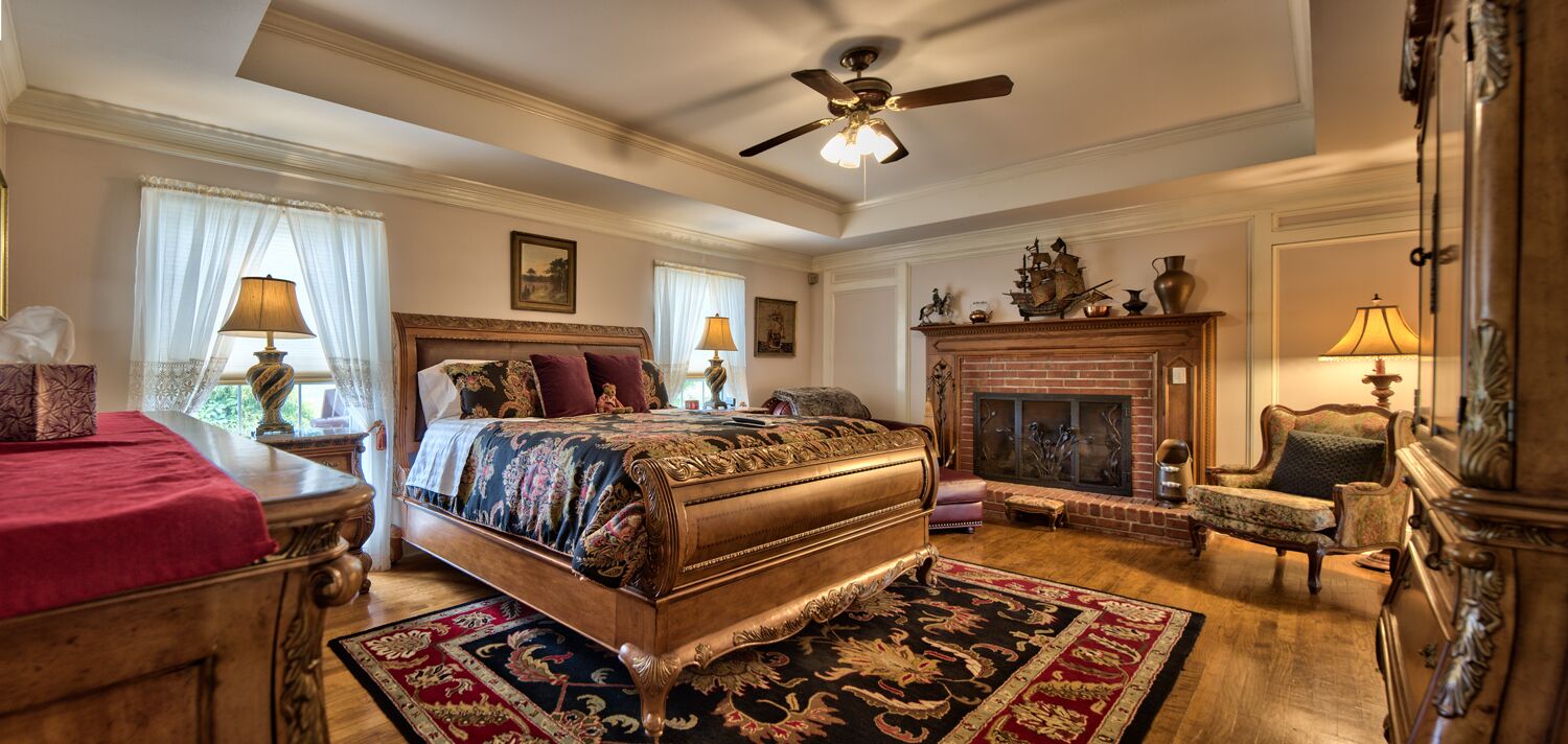 A spacious bedroom with a large bed, a fireplace, and classic decor.