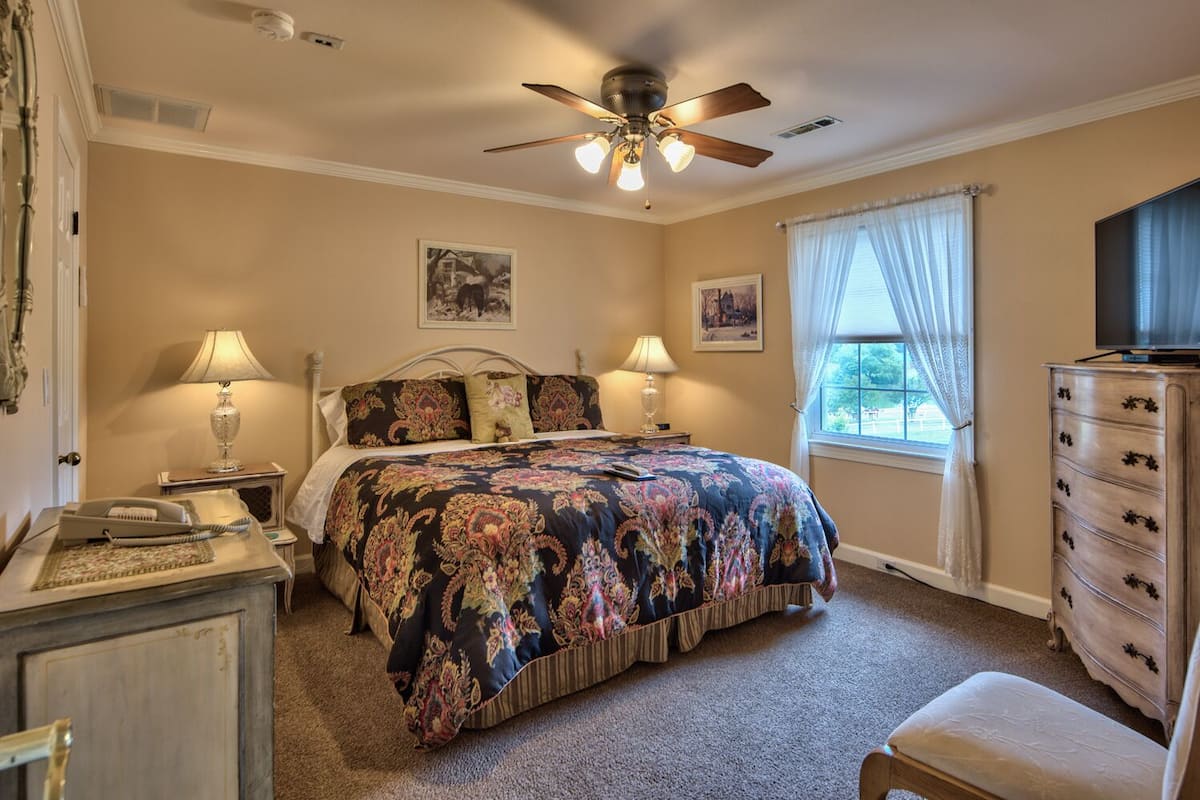 Une chambre à coucher comprenant un lit, deux lampes de chevet, un ventilateur de plafond, une commode et un téléviseur.