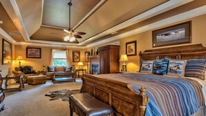 A spacious bedroom with a large bed, a ceiling fan, and a fireplace.