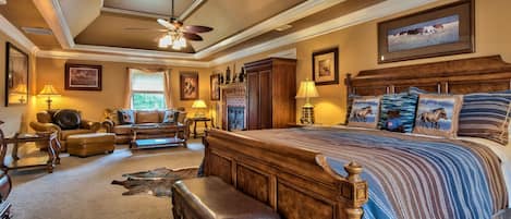 A spacious bedroom with a large bed, a ceiling fan, and a fireplace.