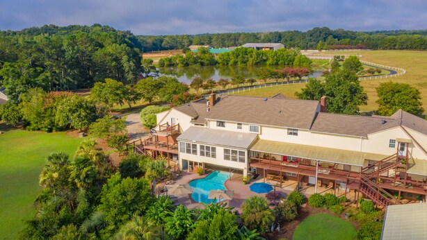 A large house with a swimming pool, surrounded by lush greenery and a lake.