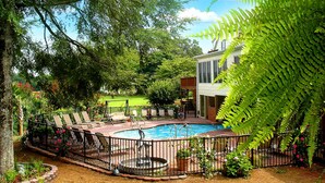 A swimming pool surrounded by a fence, with lounge chairs and a small fountain.
