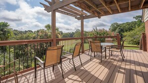 A wooden deck with a pergola, outdoor seating, and a view of a lush garden.