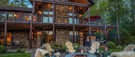 A lodge with a stone facade, wooden deck, and outdoor seating area with chairs and a fire pit.
