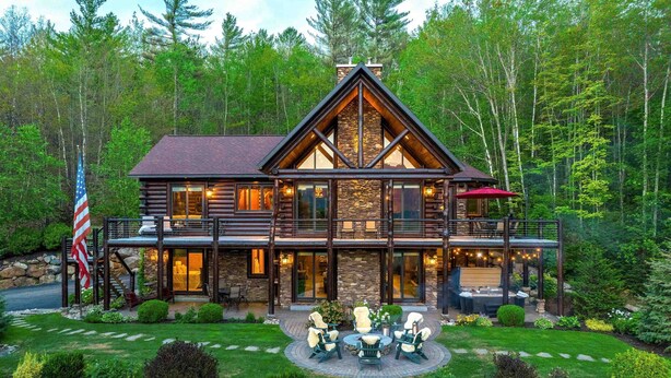 A log cabin with a stone facade, large windows, and a deck with outdoor furniture. - One-of-A-Kind Log Home in the Heart of the White Mountains NH (Intervale)