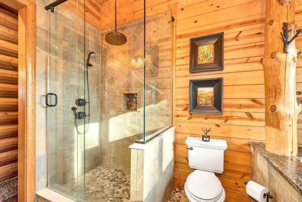 A wooden cabin bathroom with a glass-enclosed shower, a toilet, and framed artwork on the wall.