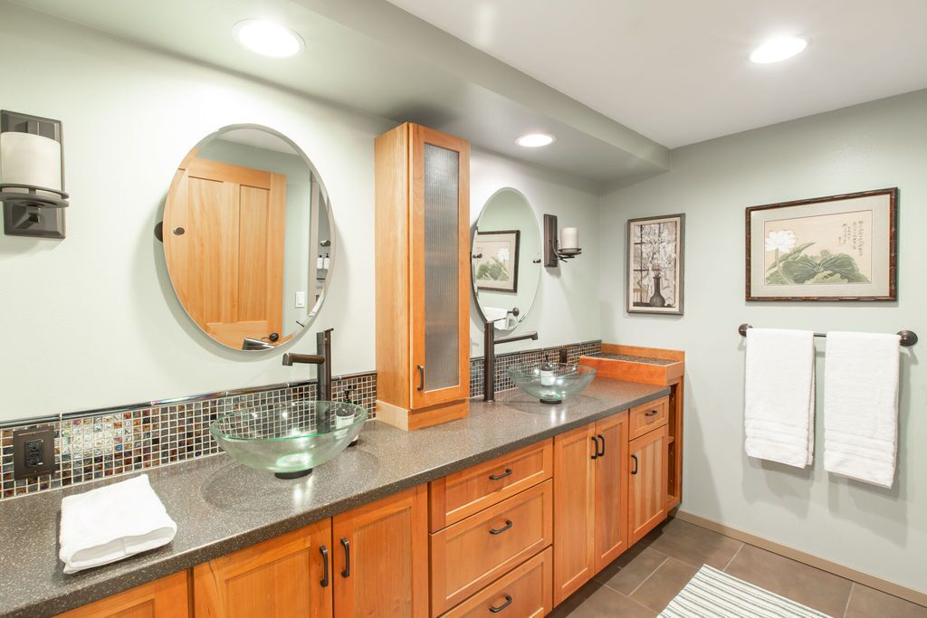 A bathroom with a glass bowl sink, wooden cabinets, and a tiled backsplash.