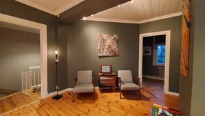 A room with wooden flooring, two grey armchairs, a small table with a picture frame, and a painting on the wall. - Historic Villa in the heart of Gränna (Jönköpings län)