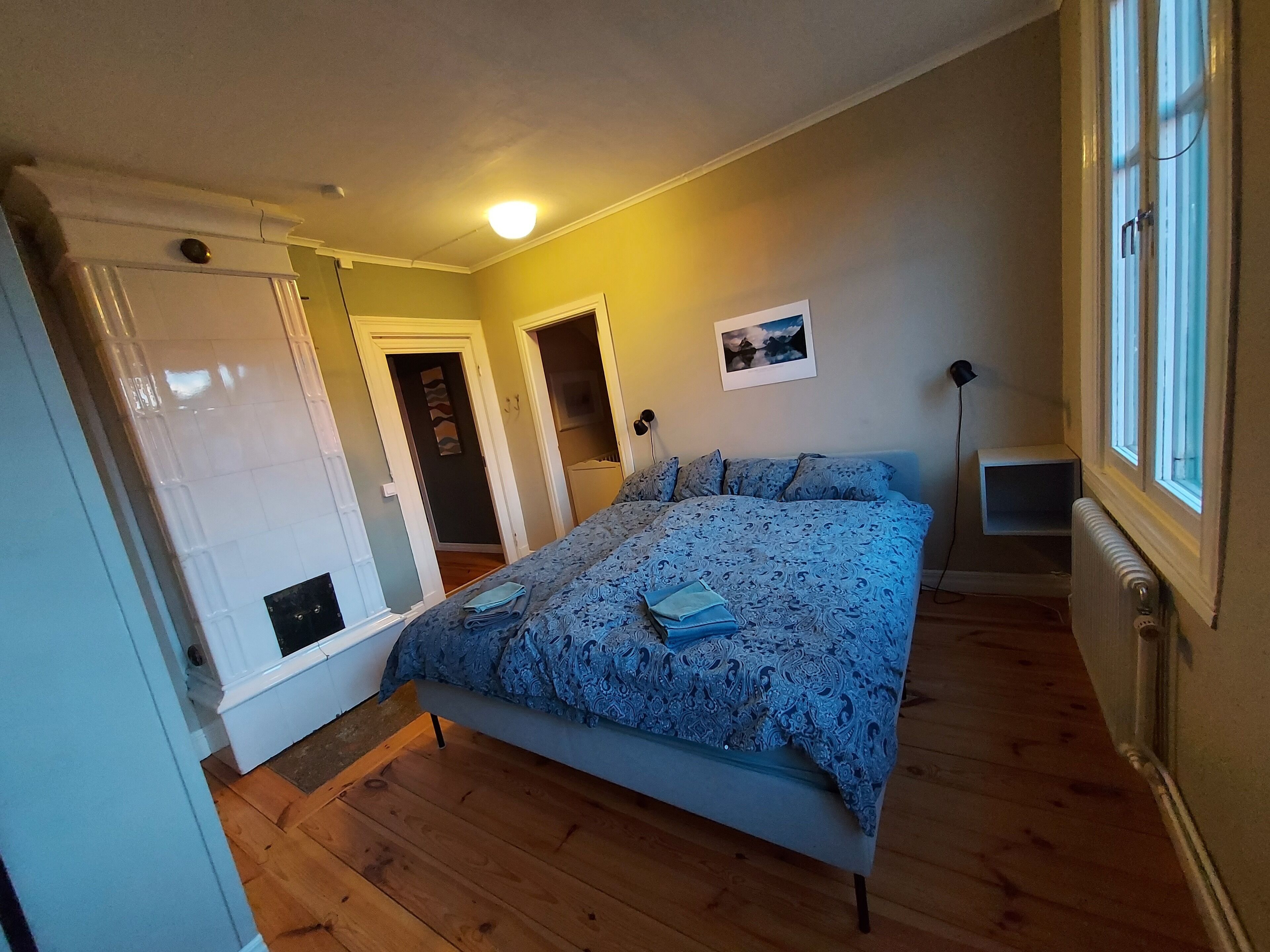 A bedroom with a bed, a radiator, a window, and a door.