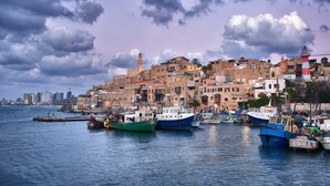 Un pueblo costero con edificios históricos, un faro y barcos amarrados en el puerto.