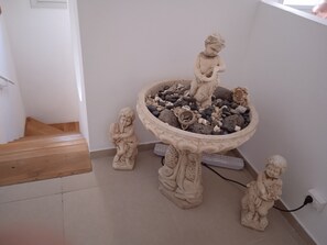 A statue of a child holding a fish, a stone basin with rocks, and a staircase.