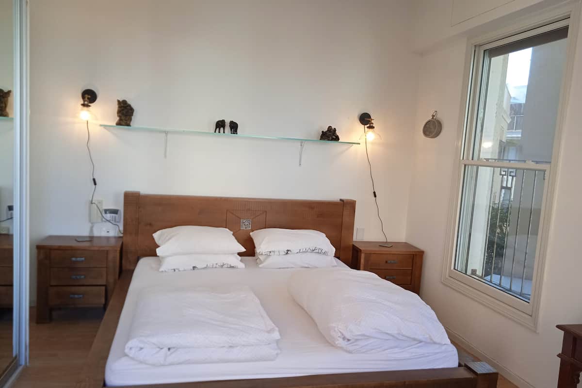 Ein ordentlich bezogenes Bett mit weißen Leinen, ein Holz-Kopfteil, Nachttische mit Lampen und ein Regal mit Dekoration.