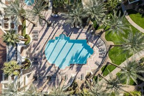 Luftaufnahme eines Resorts mit großem Schwimmbecken, umgeben von Palmen und einem gepflegten Rasen.