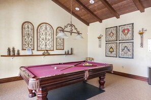 A pool table with a wooden frame and a pink felt surface, surrounded by decorative wall sconces and framed artwork.