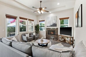 A living room with a sofa, armchairs, a coffee table, a fireplace, a TV, and a ceiling fan. - Exclusive Resort Haven | Private Pool Tennis & Spa (La Quinta)