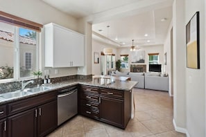A modern kitchen with dark cabinetry, a granite countertop, and a built-in dishwasher. - Exclusive Resort Haven | Private Pool Tennis & Spa (La Quinta)