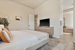 A bedroom with a bed, a dresser, a television, and a bathroom visible through an open door. - Exclusive Resort Haven | Private Pool Tennis & Spa (La Quinta)