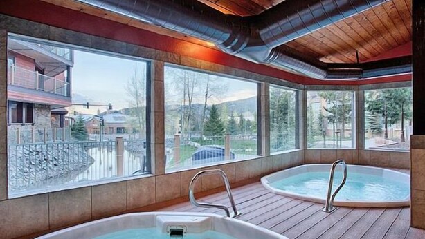 A spa area with two hot tubs and large windows offering views of a lake and buildings. - Breck-Ski IN Condo⛷Main Street 🏔 Views 😴 sleeps 8! $0 Cleaning fee (Breckenridge)
