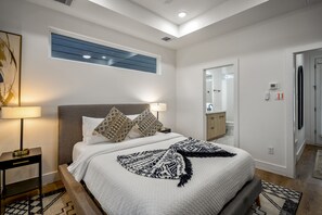 A modern bedroom with a large bed, bedside lamps, a window, and a bathroom visible through an open door. - Nestled Nook Studio #2 - 4 km from FIFA Fan Fest (Houston)