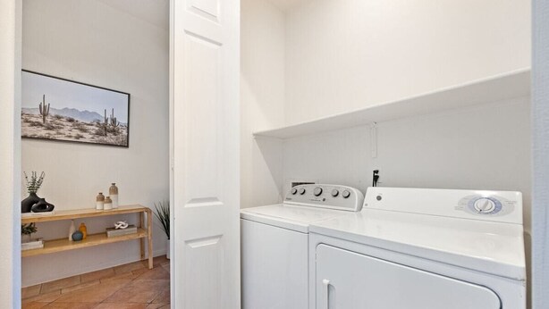 A laundry room with a washing machine and dryer, a wooden shelf with decorative items, and a framed picture on the wall.