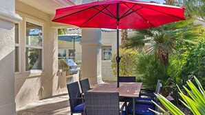 An outdoor patio with a table and chairs, a red umbrella, and a grill.