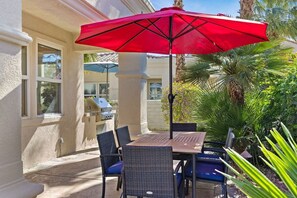 An outdoor patio with a table and chairs, a red umbrella, and a grill.