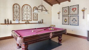 A pool table in a room with wooden beams on the ceiling, decorative wall sconces, and framed artwork.