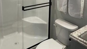 Een badkamer met een douche met glazen wand, een toilet en een handdoekrek met twee handdoeken.