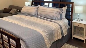 Een verzorgde slaapkamer met een bed, nachtkastje, lamp en een raam met gordijnen.