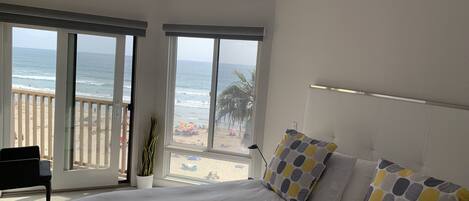 A bedroom with a large bed, a view of the beach, and a balcony.