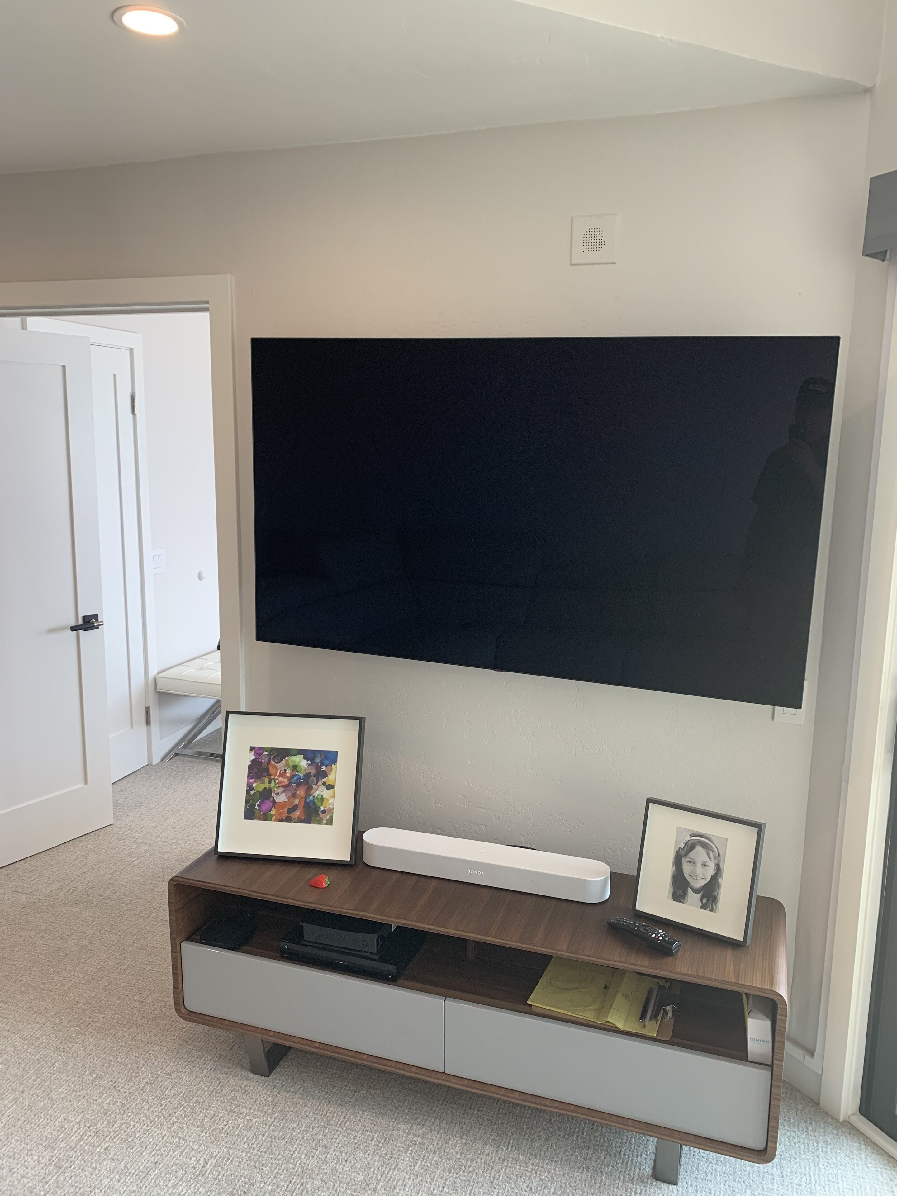 Una sala de estar moderna con un televisor de pantalla plana grande montado en la pared, un mueble de madera debajo y una puerta que da a otra habitación.