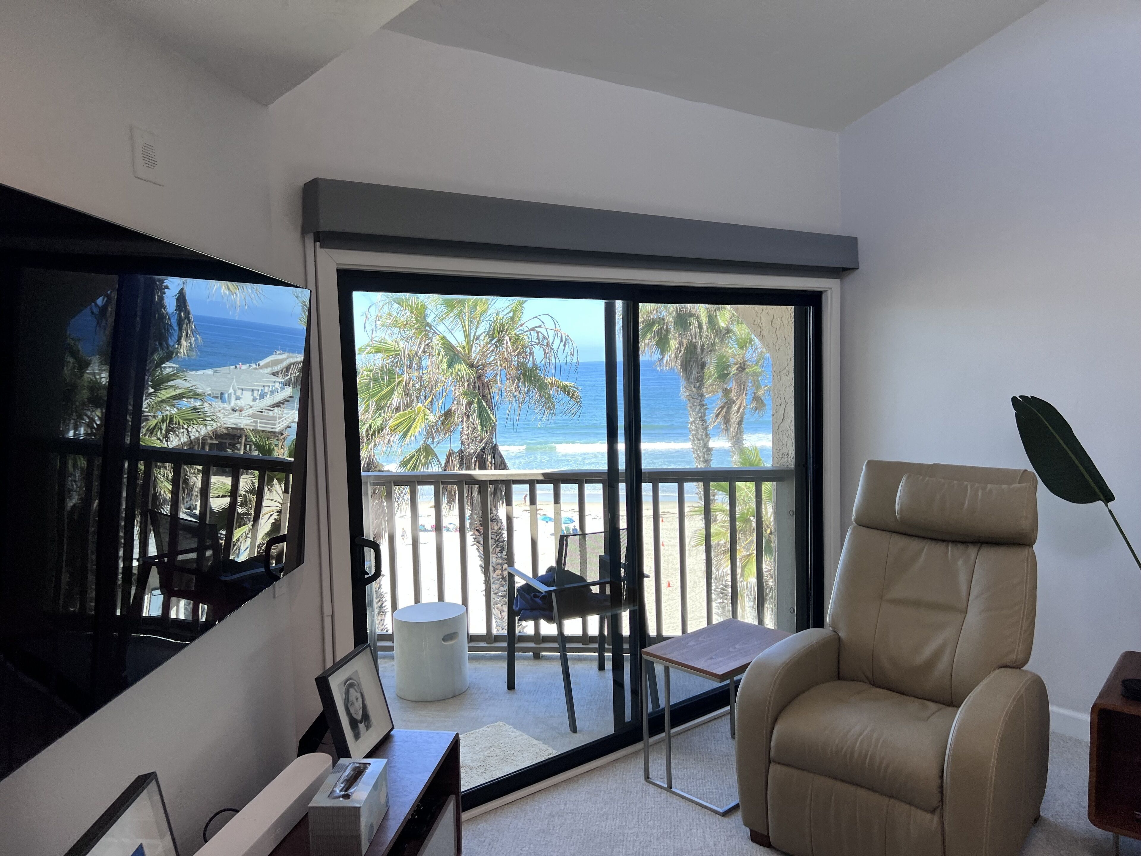 Een moderne woonkamer met een grote schuifpui naar een balkon met uitzicht op het strand.
