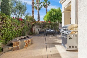 An outdoor patio with a stone fire pit, a grill, and a seating area.