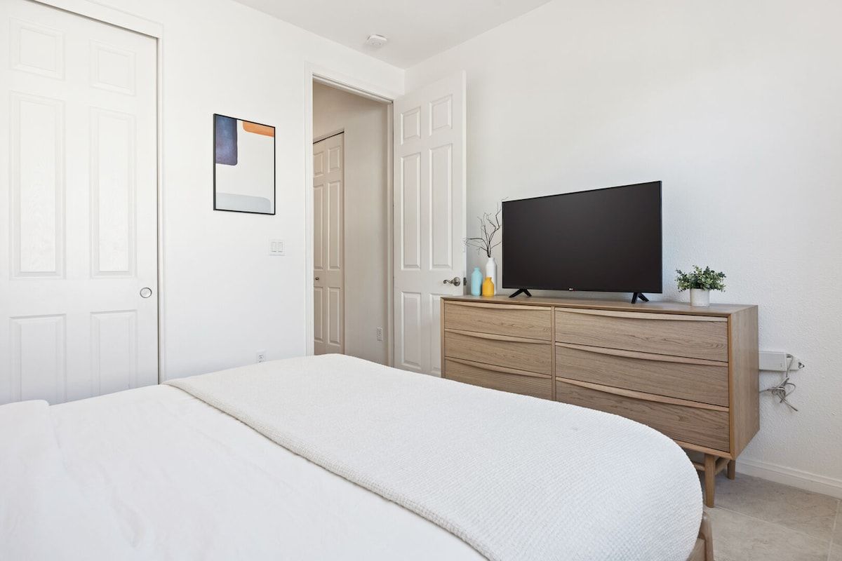 A bedroom with a bed, a dresser, a television, and a door.
