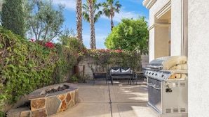 An outdoor patio with a stone fire pit, a grill, and a seating area with a bench and chairs. - Experience luxury at Desert Retreat, a haven in La Quinta, near PGA West. (La Quinta)