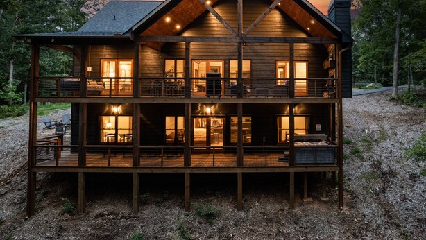 A two-story log cabin with a balcony, multiple windows, and a fireplace visible inside. - Hot Tub- Modern Luxury -5 Bdrm-4 Kings- Pool Table (Blue Ridge)