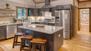 A modern kitchen with a large island, stainless steel appliances, and wooden bar stools. - Hot Tub- Modern Luxury -5 Bdrm-4 Kings- Pool Table (Blue Ridge)