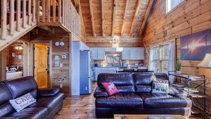 A cabin interior with a wooden interior, a kitchen, and a living area with leather sofas. - Sunset-View 3BR Blue Ridge Cabin • Hot Tub (Cherry Log)