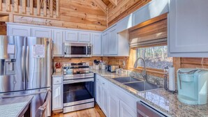 A modern kitchen with stainless steel appliances, granite countertops, and wooden ceiling beams. - Sunset-View 3BR Blue Ridge Cabin • Hot Tub (Cherry Log)