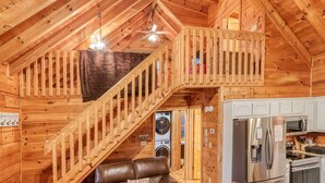 A cabin interior with a wooden staircase, a kitchen area, and a laundry room. - Sunset-View 3BR Blue Ridge Cabin • Hot Tub (Cherry Log)