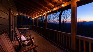 A wooden deck with string lights, a table, and chairs. - Sunset-View 3BR Blue Ridge Cabin • Hot Tub (Cherry Log)