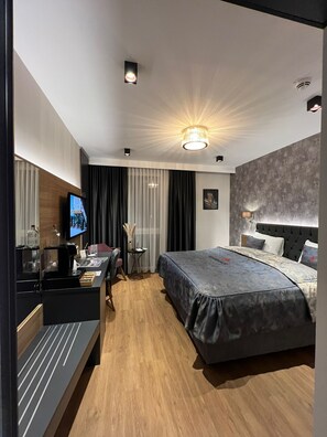 A modern hotel room with a large bed, a desk with a coffee machine, a TV, and a minibar. - Hotel Winterrot (Karlsruhe)