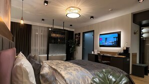 A modern bedroom with a large bed, a TV, and a plant. - Hotel Winterrot (Karlsruhe)